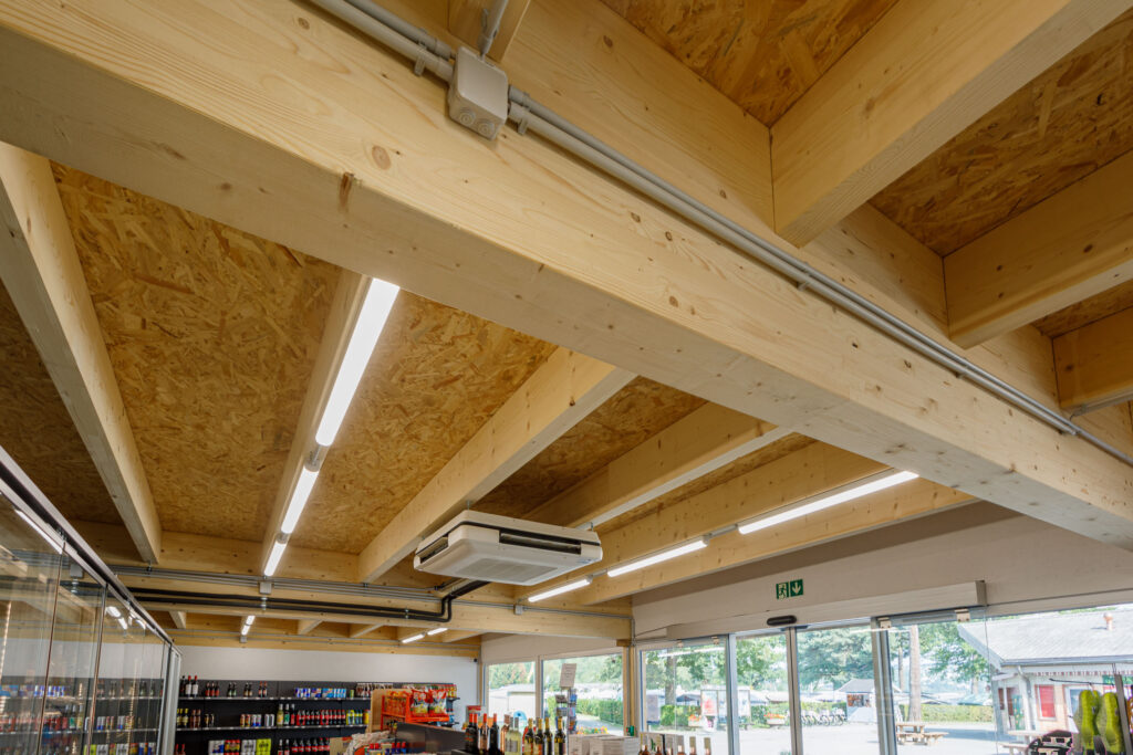 Vue intérieure du magasin du Camping Plage à Avenches avec charpente en bois apparente.