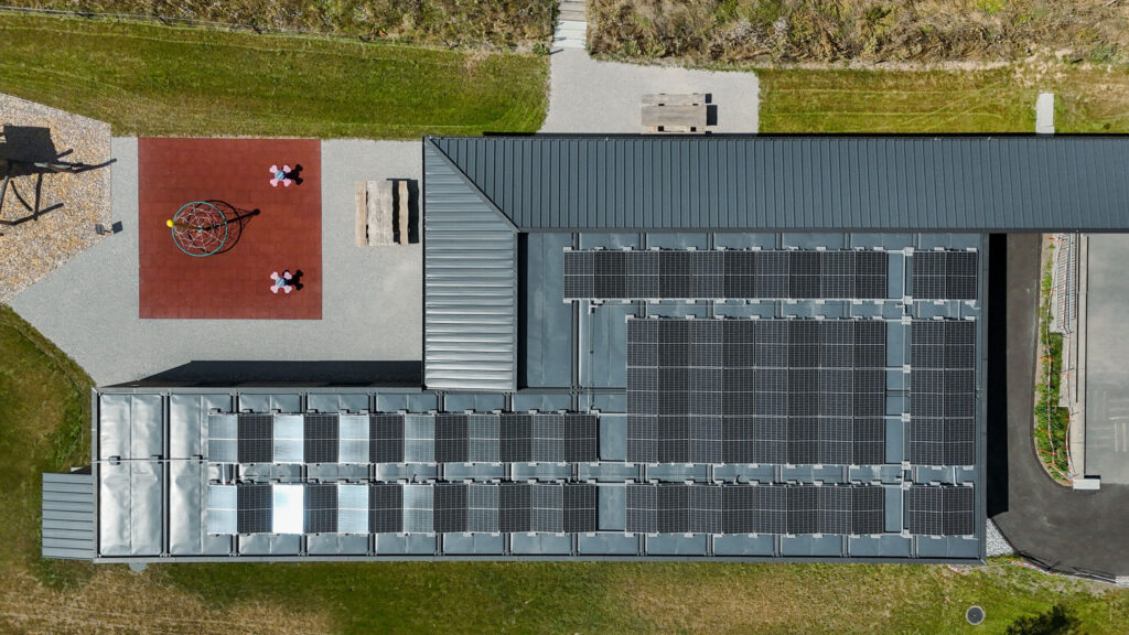 Axiale Luftaufnahme des Dachs der Primarschule in Lossy mit Photovoltaikanlage.