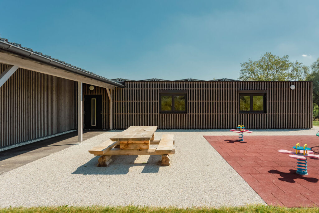 Pausenplatz der Primarschule in Lossy mit Holzbänken und Holzverkleidung am Schulgebäude.